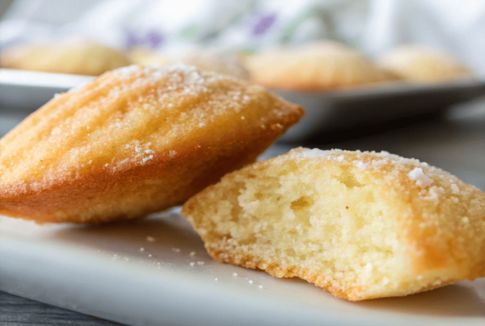 Close-up of soft and fluffy madeleine cookies with a golden-brown crust, dusted with powdered sugar.