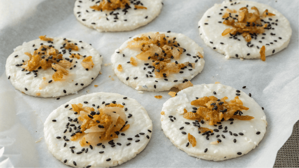 rounds of cottagecheese spinkled with black sesame seeds and crispy fried onions, arranged on parchment paper.