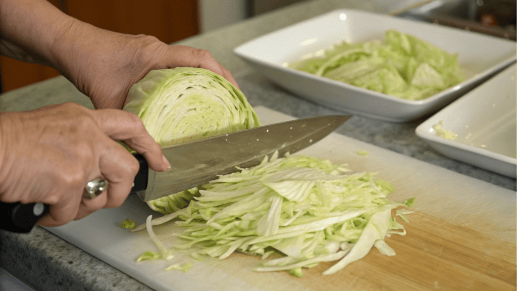 Close-up of hands slicing fresh cabbage on a cutting board for Coal Miner’s Recipe for Sauerkraut.