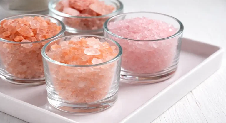 Three small clear glass cups filled with pink Himalayan salt crystals in different shades, arranged on a white tray with a soft neutral background.